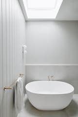 Freestanding bathtub and brushed brass fixings provide contrast and visual interest against grey tiles and paneling.