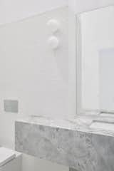 Powder room featuring wall mounted lights, penny round tiles and marble counter.