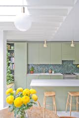 The architects replaced the existing small and dark kitchen with an open-plan cooking and dining area that includes floor-to-ceiling windows and a skylight. Muted earth tones, such as the olive-green cabinets and jade tile backsplash, mimic the hues of the greenery outside.&nbsp;&nbsp;