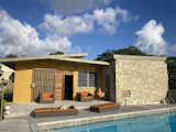 AFTER.  View from pool after the renovation. Large openings were filled with Mahogany louvre doors and security, louvre windows. Plaster wall was painted mustard and trim with taupe. A new concrete paved patio was installed.