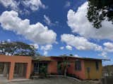 AFTER (View from driveway.) Warm salmon color used for the exterior of the core of the house on the driveway side. The round arches were squared and fenced providing security as well as visual separation. Pool beyond, out to the right. A banana tree bears fruit every year.