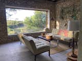 AFTER. Main living room, with oversized window looking out into small tropical forest and hillside beyond. Iconic stone walls, terrazzo floors.  Large felt roll ("skeleton") used to soften the concrete bench at window brought from Hudson Valley. Fishing nets on stone wall.