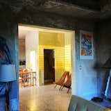 AFTER. View from living room toward dining area and kitchen. Raw concrete walls with yellow patina.  Terrazzo floors. Art by author.