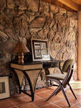 A midcentury modern bamboo and rattan writing desk with a Louis Van Teeffelen chair rests against the original faux rock walls.