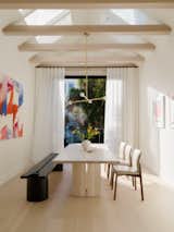 In the reimagined earthquake shack, a brass pendant from Allied Makers is suspended above a bleached ash dining table. In the background, the backyard beckons through the enlarged glazing.