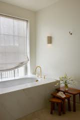 Primary bathroom with brass fixtures, marble clad tub and linen shades. 