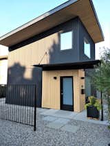 Side entrance highlighted in Hemlock planks. The corrugated metal siding has a matte black 'rawhide' textured finish.