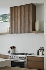 Kitchen, Engineered Quartz Counter, Stone Slab Backsplashe, Range, Wine Cooler, Light Hardwood Floor, White Cabinet, Recessed Lighting, Dishwasher, Range Hood, Undermount Sink, Wood Cabinet, and Ceiling Lighting Kitchen hood fan  Photo 17 of 27 in The Avondale Home by Art & Stone Group