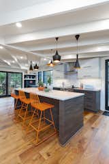 Grey lower cabinets, white upper cabinets with painted white beams and pops of orange enliven the space. Large metal sliding doors invite the outside in. 