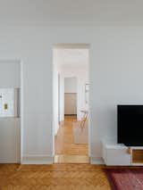 The central corridor guides guests between the central dining area and the living room. Diagonal herringbone wood flooring is present throughout the home.  Photo 7 of 13 in You’ll Either Love or Hate This Renovated Lisbon Flat’s Wooden Cabinet Pulls
