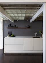 The crisp, white kitchen counters sit below an open shelf showcasing ceramics made by Diana.