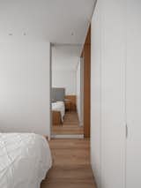 Bedroom, Medium Hardwood Floor, Ceiling Lighting, and Bed A mirror, blended in the wall, creates an amplitude where none existed before, and the pivoting door acting as a large plane, allows us to enclose the space, or guarantee the desired fluidity and permeability, when open.  Photo 13 of 28 in Capitaes Abril apartment by estudio AMATAM