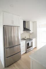 Kitchen, Engineered Quartz Counter, Wood Cabinet, Refrigerator, Range Hood, White Cabinet, Light Hardwood Floor, and Range  Photo 5 of 12 in The Lookout by The Lookout