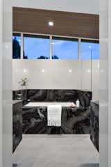 Bath Room, Undermount Tub, Porcelain Tile Floor, Ceiling Lighting, Stone Slab Wall, and Engineered Quartz Counter Primary Bath  Photo 12 of 16 in Monarch by Liz Reid