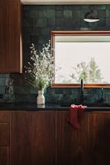 Green tile backsplash, walnut cabinetry, black granite counters, black plumbing and black lighting fixtures. 