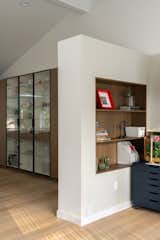 The partial-height wall acts as both a functional separator and a design element, preserving the sense of openness while framing a custom-built niche that houses shelving for the office and art materials, seamlessly blending functionality with the surrounding space.