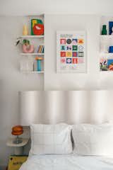 The peaceful white walls of the bedroom juxtapose vibrant colors up top on the wall shelves. The poster is from Gustav Westman and the headboard is from Urban Outfitters.