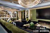 A generous, custom sectional draped in dark green and black sultry velvets, anchors the primary seating area. A black lacquer and brass coffee table from the Lori Morris collection and custom black velvet club chairs with brass accents, complete the vignette, gathered around a fireplace and oversized TV wall, clad in green back painted glass and brass strapping.