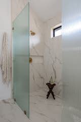 Primary bathroom shower with marble tile, gold hardware, and a large niche