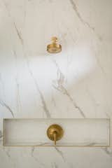 Primary bathroom shower with marble tile and gold hardware