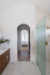 Primary bathroom shower with marble tile and gold hardware looking into the primary bedroom