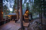 Twilight Photo of the front of the cabin. As you drive up, you are met by a dramatic black cabin with an expansive cedar deck. The warm string lights are a precursor to the cozy home you are about to enter.