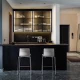 Dry kitchen and bar area are designed to add texture with solid black Kadappah stone counters, laminated cabinets and reeded glass wall shutters. Seen to the right in the entryway into the home from a private elevator. 