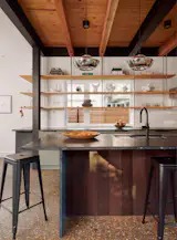 The architects brought more light into the kitchen by including a window behind the sink. It wasn’t a nice view, so they installed open shelving in front of it: birch plywood attached to threaded rods hung from structural wood and steel.
