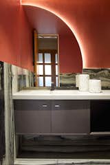 A powder bathroom tucked beside the home theatre gives a sense of innate drama with a black and white patterned marble on its floor and walls till mid-level. The rest of the wall is painted in a rich burgundy hue. The curved backlit mirror heightens the drama with a counter built on site.