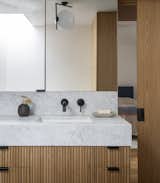 The materials-forward primary bathroom features additional custom oak cabinetry and a thick marble countertop. Minimal hardware and a geometric overhead light are subtle yet sophisticated additions. 