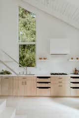 The previous galley-style kitchen was dark and closed off from the rest of the house. For the remodel, Sammie requested high ceilings, no upper cabinets, and U-shaped drawers. Simple white-painted upper shelves display a collection of ceramic dishes. 