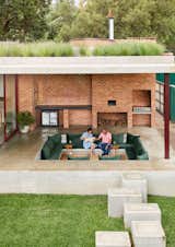 Homeowners Toni and Graeme sit on the patio with their dog Bokkie. An exterior conversation pit is the most popular spot in the house. A gas grill and pizza oven are built into the back brick wall. The countertop to the left of the wood storage nook is made with leathered Zimbabwean Granite.