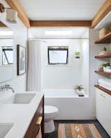 White-painted shiplap in the bathroom brightens the room, while wood details such as the oak ceiling trim and walnut vanity and shelving add warmth to the palette. 