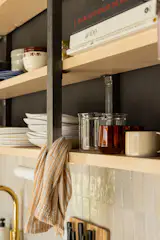 The kitchenette is compact but effective. The shelving unit had to be anchored to the ceiling; building codes required a bannister for the loft, so Ben rigged up a two-for-one design. The terracotta backsplash tile is from Clé and the brass fixtures are by Phylrich.