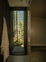 In the primary bathroom, a simple palette of concrete floors and dark-stained cedar falls to the background, allowing the trees and stumps outside—seen through a purposefully placed window—to take center stage.