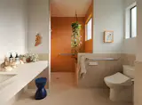 For her parents' bathroom, Bhavani pushed them towards this orange tile, noting that "usually [they] love all white." Adaptive measures—a curb-less shower, grab bars, and a built-in bench—allow for independence while aging in place. The floor and wainscoting are porcelain terrazzo. 