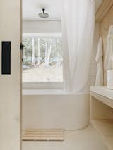 An insulated, freestanding tub with a picture window onto the forest is the main feature of the bathroom, which also incorporates the same materials used throughout the space–birch plywood, white concrete, and shiplap.