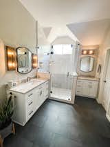 Slate black tile bathroom floor , white contemporary shower with quartz waterfall ledge. White vanities. Champagne bronze plumbing fixtures 