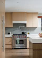 Cabinetry with integrated pulls showcase the wood species in their natural splendor; a contrast color island in walnut anchors the space, tied to the walnut flooring and visually supporting the weight of the 6” stone counter atop.