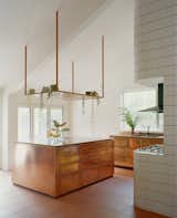 Plants spill over the steel shelf above the copper-covered island bench, adding to the kitchen's cocktail bar vibe.