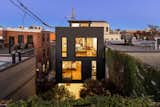 Rear of home at twilight, as seen from a rooftop beyond the property. The ground floor is a guest suite and garage, the second floor contains two bedrooms and two baths, the upper floor is open concept living space with 14' clerestory. The scale of the home is hidden from the narrow alley street and the rear of the home is an enclosed garden.