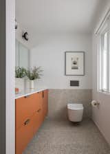 The primary bath, with terrazzo flooring becoming the wainscot behind the wall-hung toilet.  A two-tone vanity adds a splash of color. 
 A wall to wall mirror conceals the medicine cabinet. 
