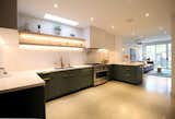 The kitchen features quartz surfaces, oak shelving, white and green cabinetry, and a polished concrete floor.