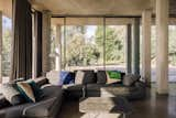 A gray sofa is dappled in sunlight from the surrounding window walls.