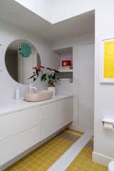 A mirror by Ghislaine Viñas hangs over the Kast sink in the expanded bathroom, where the floor and shower feature mustard-colored tile by Clé.