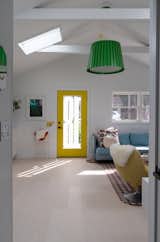 A bold green pendant by Alexander Taylor for Established & Sons hangs over the open plan kitchen and living room, sunlit through the glass front door. 