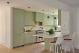 A minty pistachio hue paints the Reform Kitchen cabinetry, paired with Calacatta Gold marble countertops and the homeowner's existing Viking range. The Eames Molded Plastic bar stools sport leather pads. Lighting by Commune Design and Seed Design.