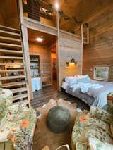 The Barn at Edenwood Tiny Home Main Level View (includes seating area with reclaimed Henredon chairs), luxe kingsized bed, efficient tiny home table for two handmade in Flat Rock, NC, kitchenette, and reclaimed 100 year old door (photo credit The Hive Drive)