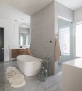 Primary bathroom with finishes and textures reminiscent of a spa. Soft curves, warm brass tones and natural walnut cabinetry add coziness to this bright airy space.