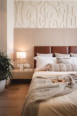 The bedroom area with the customised modern art-deco wall panel, layered with an asymmetrical fluted panel which enhances the tan leather of the bed's headboard. The bedside tables are also customised to blend with the art wall which is a familiar language throughout the whole space.